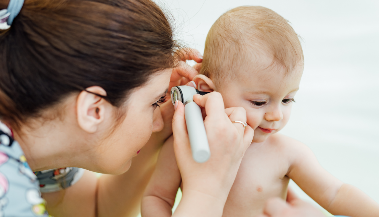 Woman pediatrician is examining little baby in clinic baby's ear diagnosing