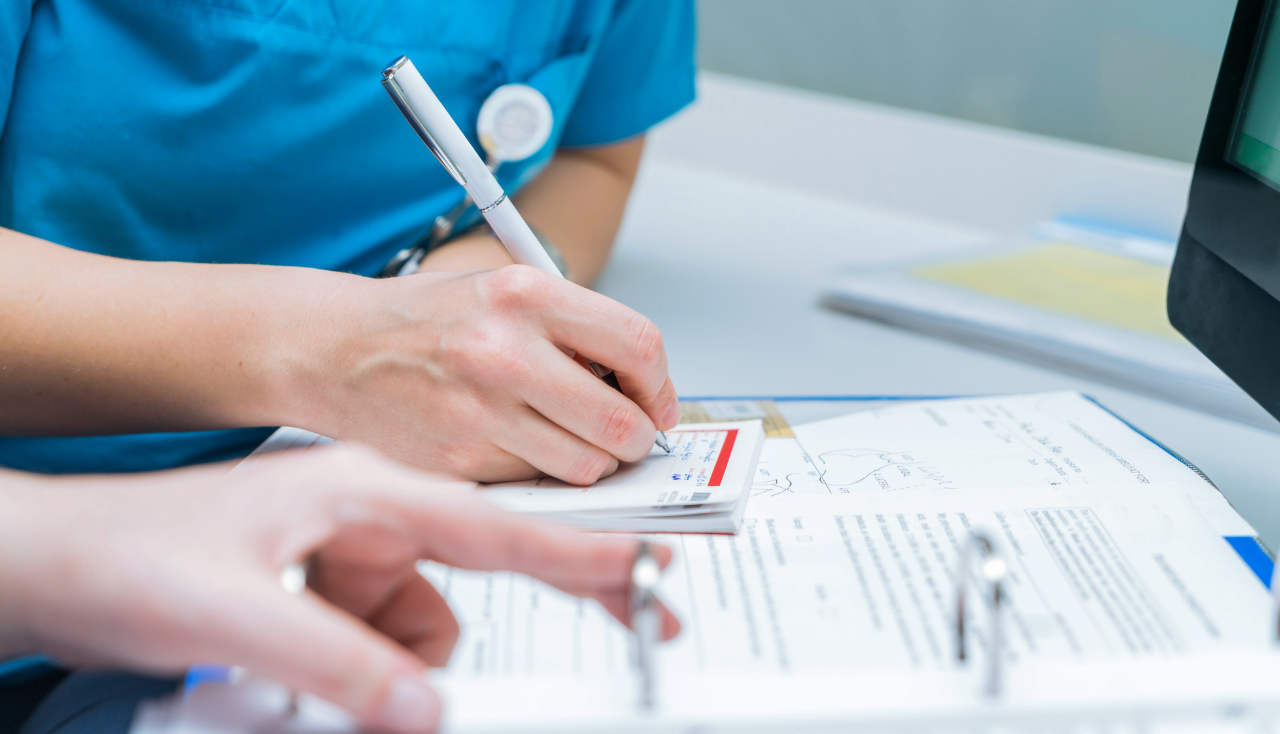two nurses share patient information by writing it on the patient file