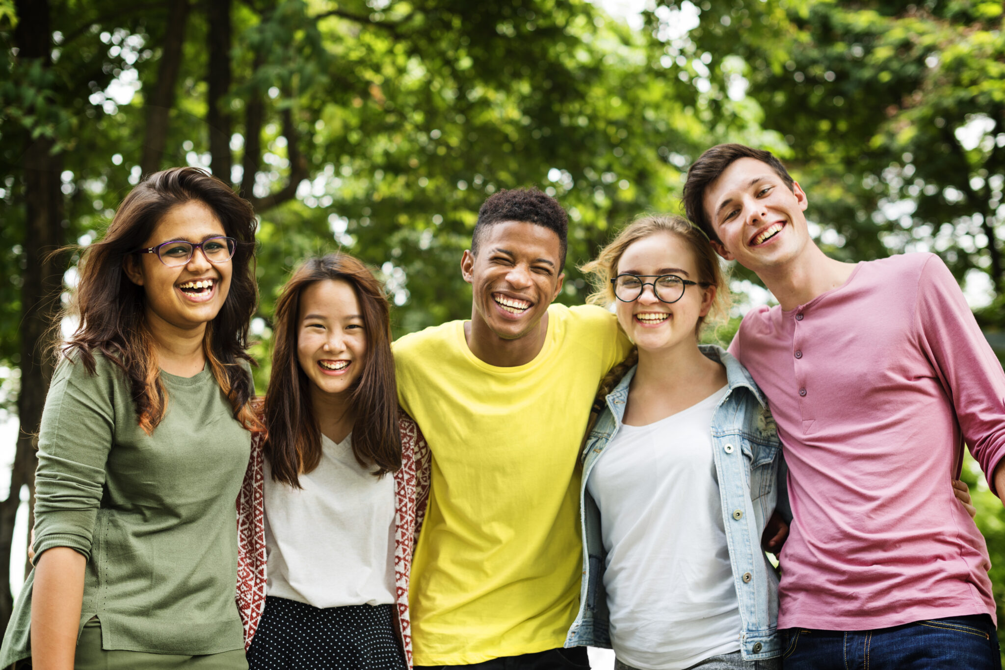 A group of five friends stands outdoors, smiling broadly.